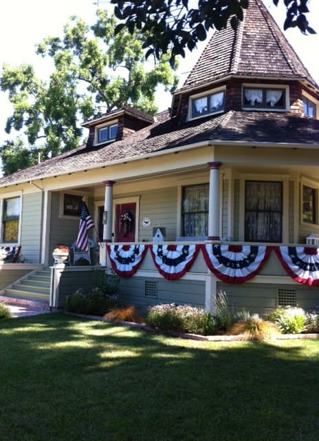 A sage-green Queen Anne house in Pleasanton, its turret and porch hung with bunting